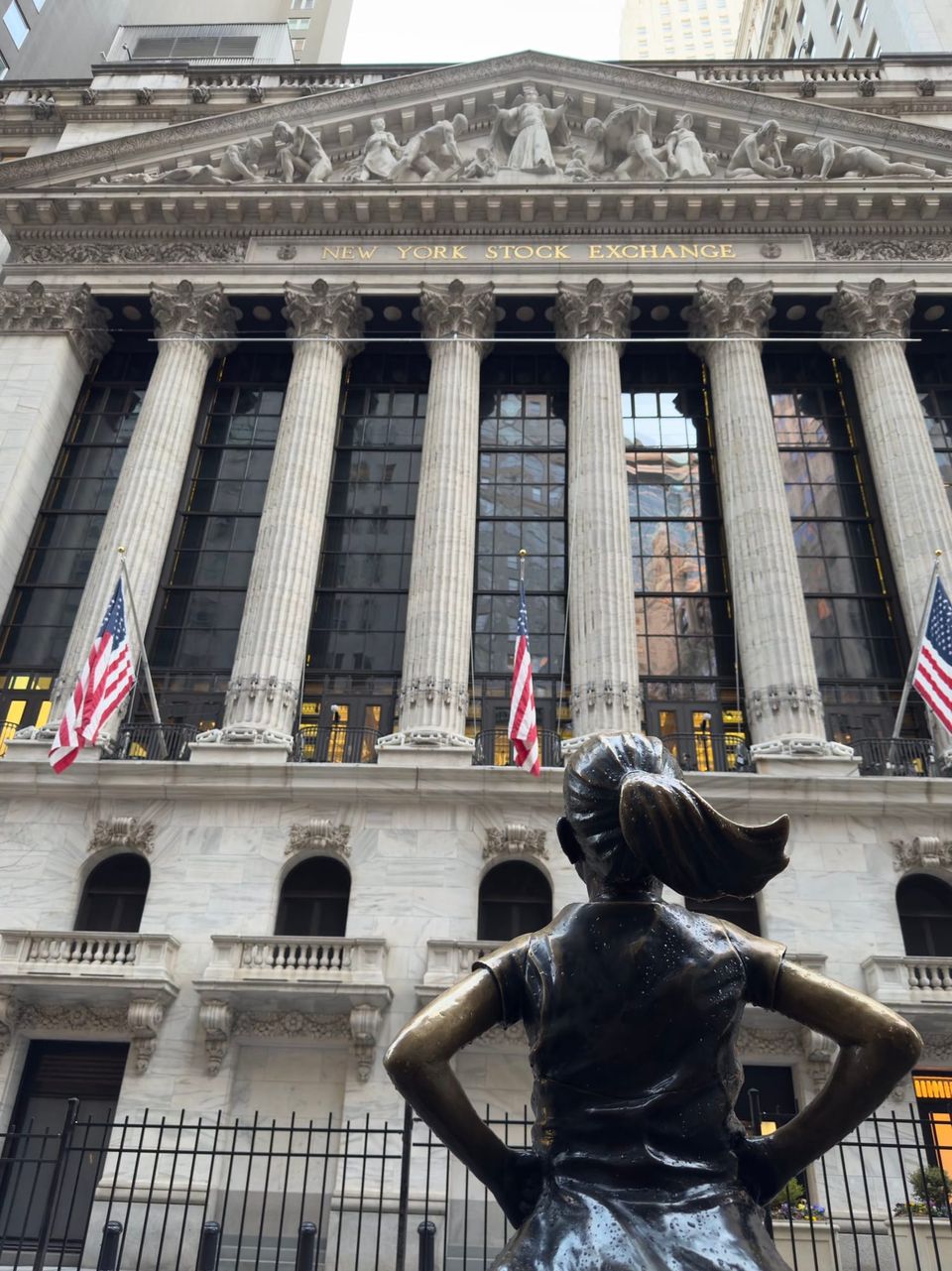 Fearless Girl statue facing the New York Stock Exchange facade with American flags