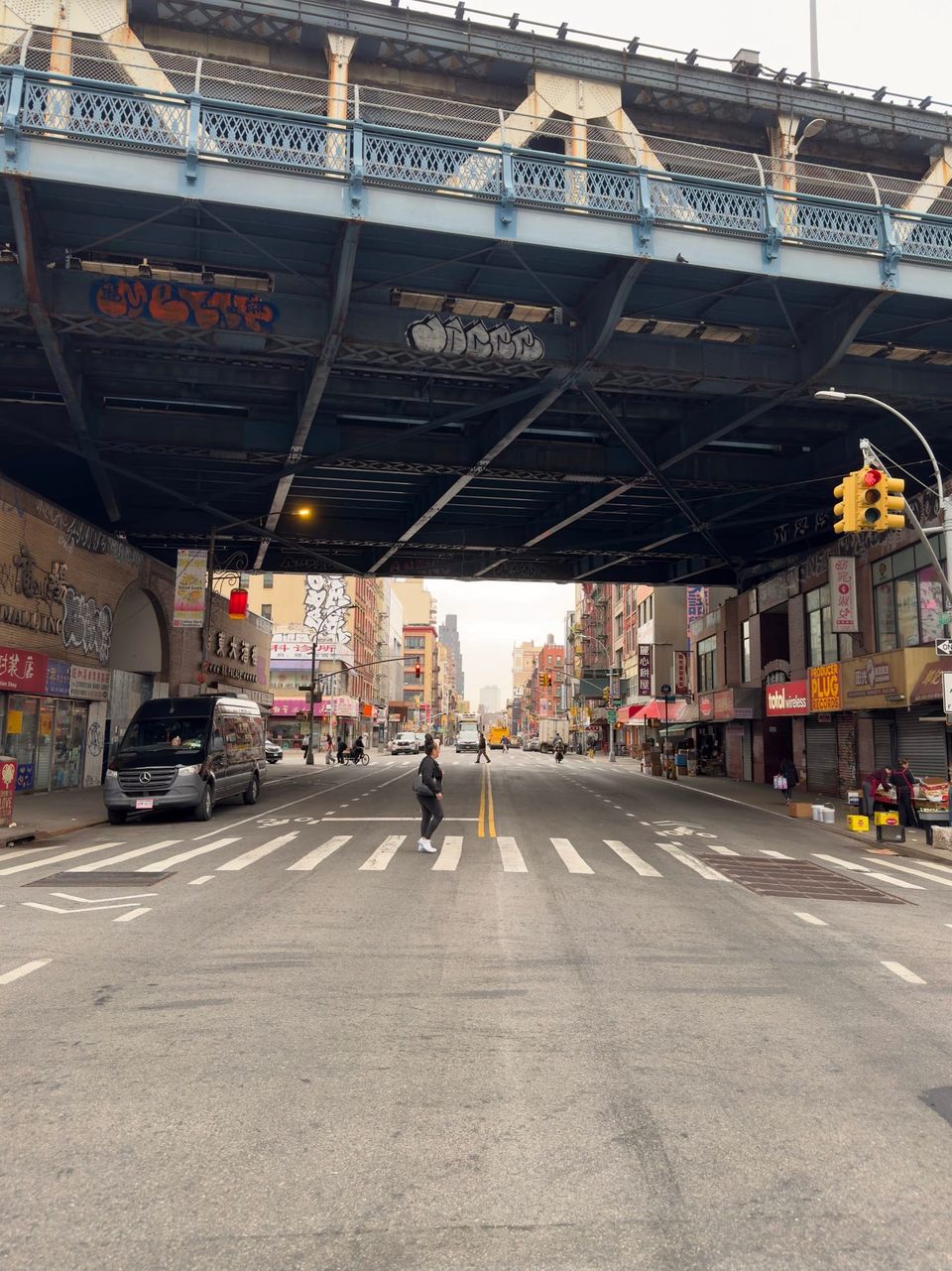 Street under the Manhattan Bridge overpass in Chinatown with a woman crossing