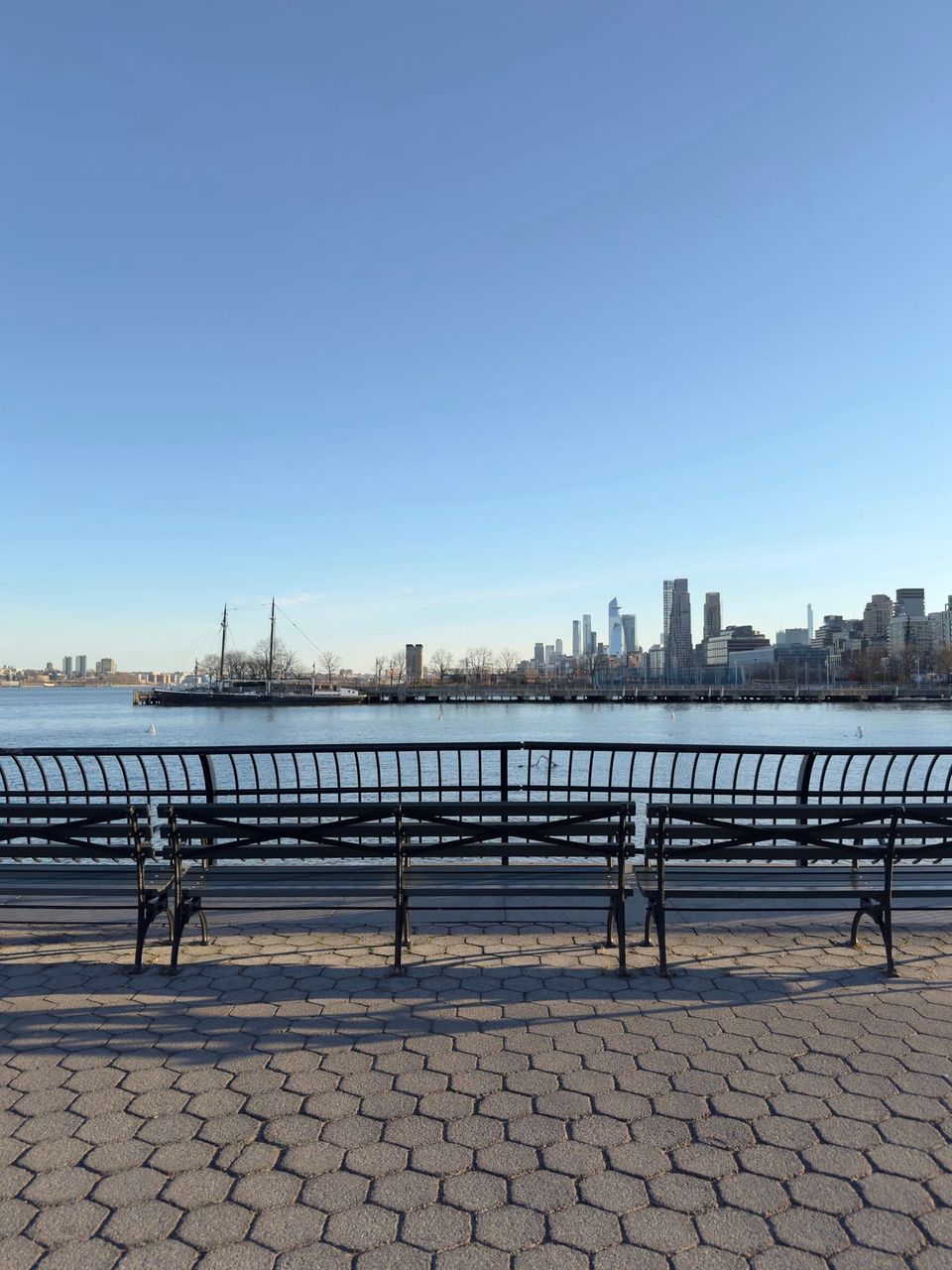 Row of benches on a Hudson River promenade facing a tall ship and Manhattan skyline