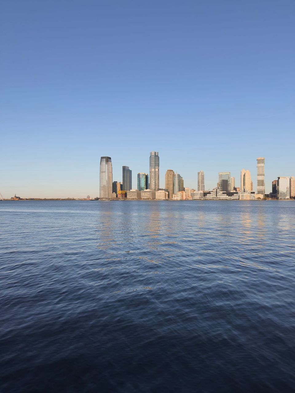 Jersey City skyline across the Hudson River under a clear blue sky