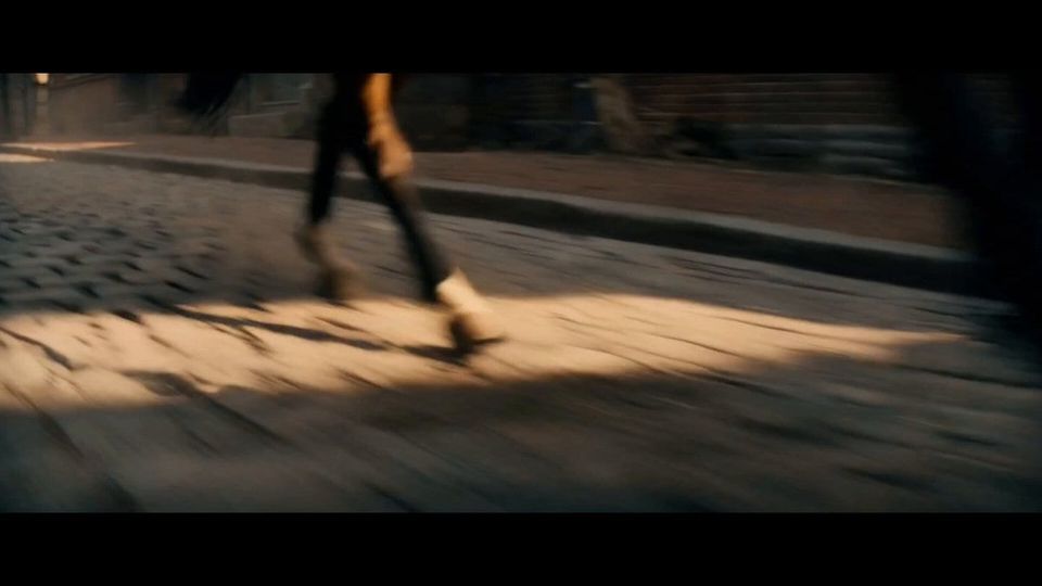 Motion-blurred film still of legs in boots running on a sunlit cobblestone street