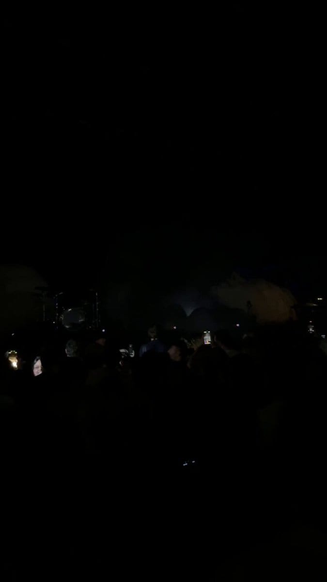 Nearly dark concert crowd with a faint stage and glowing phones