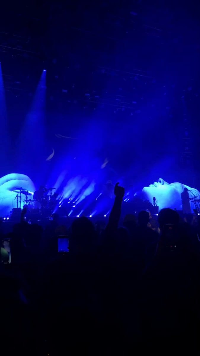 Stage bathed in blue light with giant reclining face sculptures and a raised fist in the crowd