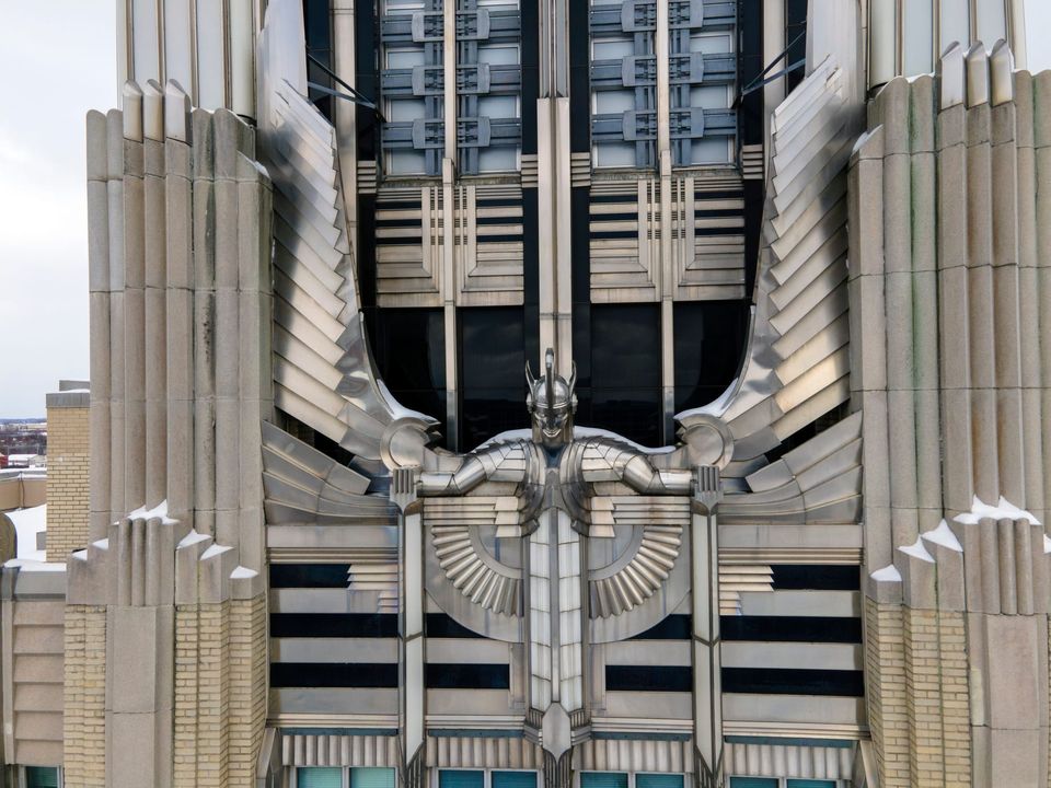 Close view of an Art Deco façade with a silver winged figure sculpture and geometric stone and metal details
