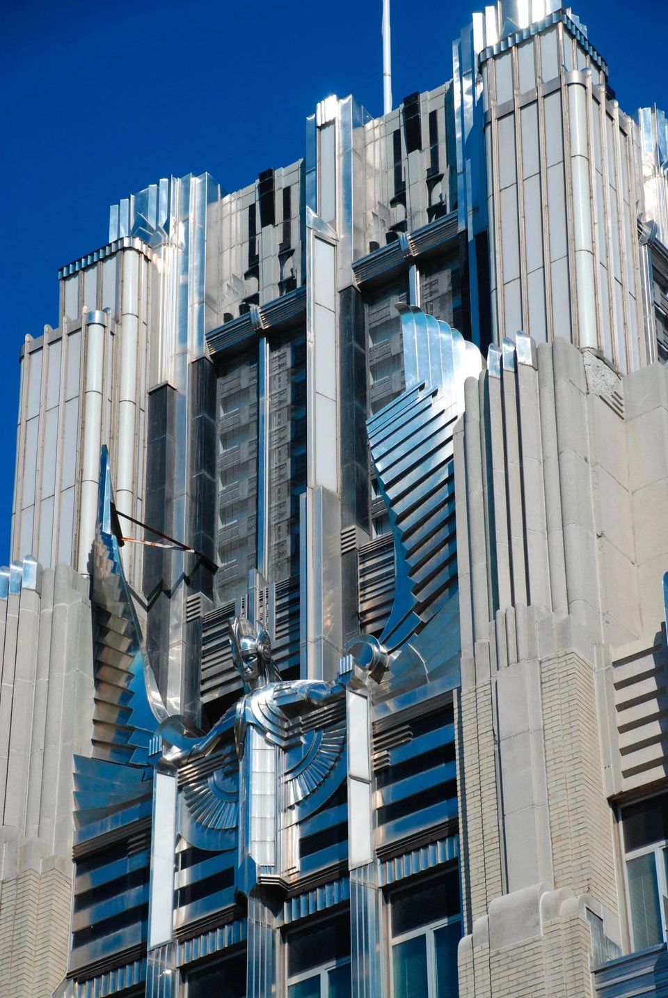 Angled view of the Niagara Mohawk Building’s reflective Art Deco façade and silver winged figure against a blue sky
