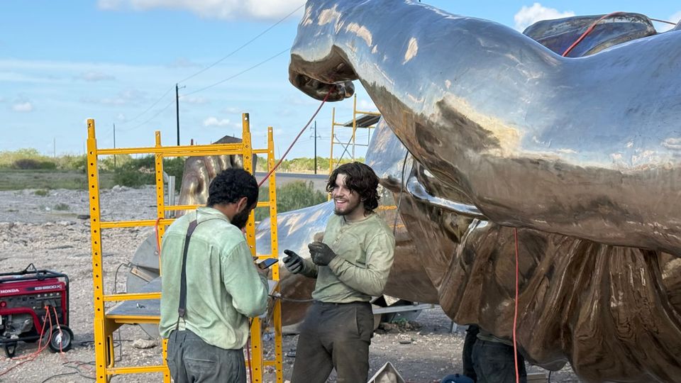 Two workers talk beside the reflective bronze statue and yellow scaffolding