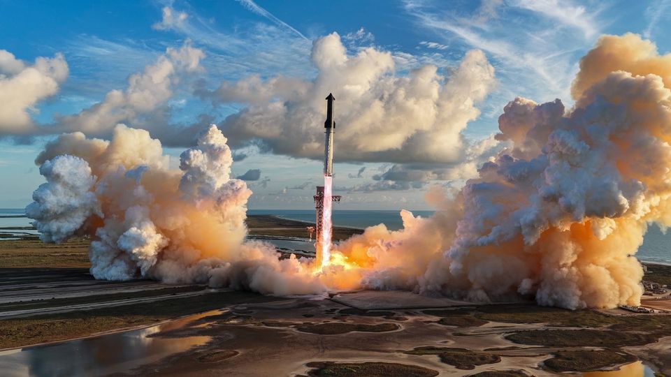 A rocket launches above a coastal landscape, surrounded by clouds of smoke and fire