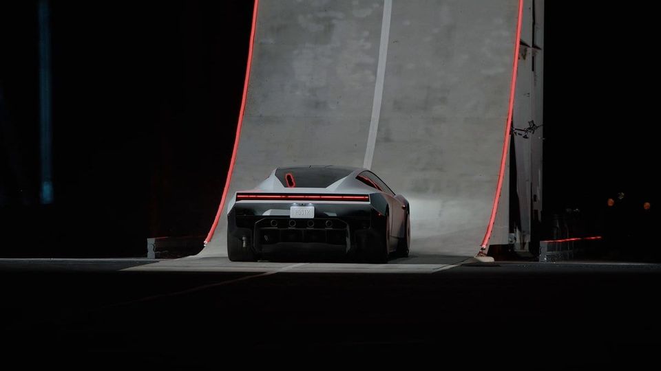 Rear view of a silver Tesla Roadster beneath a towering gray ramp outlined in red lights