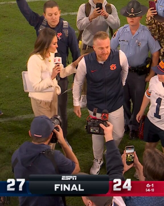 An Auburn coach and sideline reporter on the field as ESPN’s scoreboard shows FINAL, Auburn 27 and its opponent 24