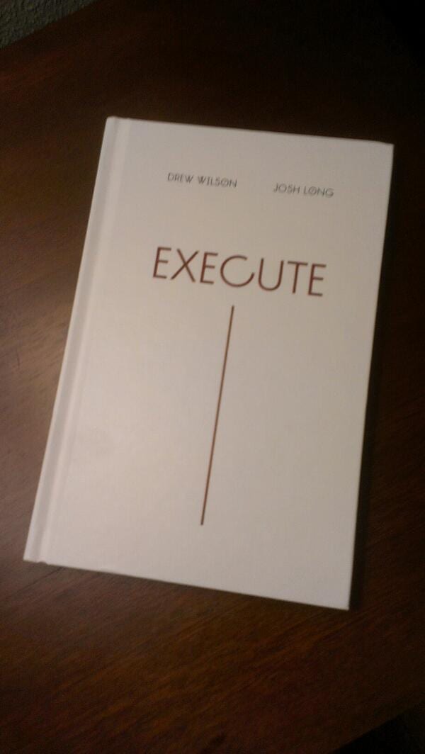 White hardcover of Execute by Drew Wilson and Josh Long on a wooden table