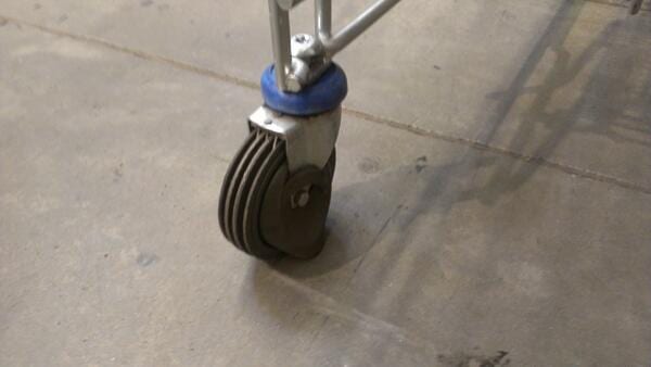 Close-up of a shopping cart caster with a multi-grooved black wheel on a concrete floor