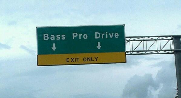 Green highway sign reading Bass Pro Drive with a yellow Exit Only banner under a cloudy sky