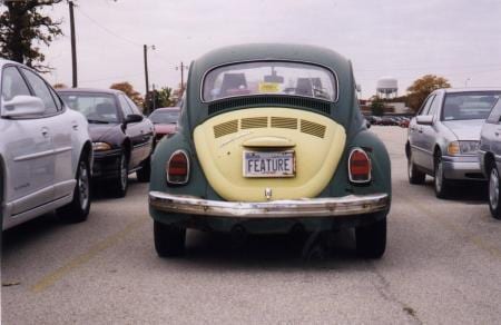Rusty green and yellow Volkswagen Beetle with a license plate reading FEATURE