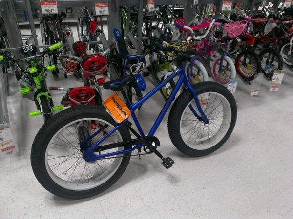 Blue Mongoose fat-tire bicycle displayed in front of rows of kids' bikes in a store aisle