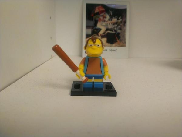 Nelson Muntz LEGO minifigure holding a baseball bat on a shelf with a Polaroid behind