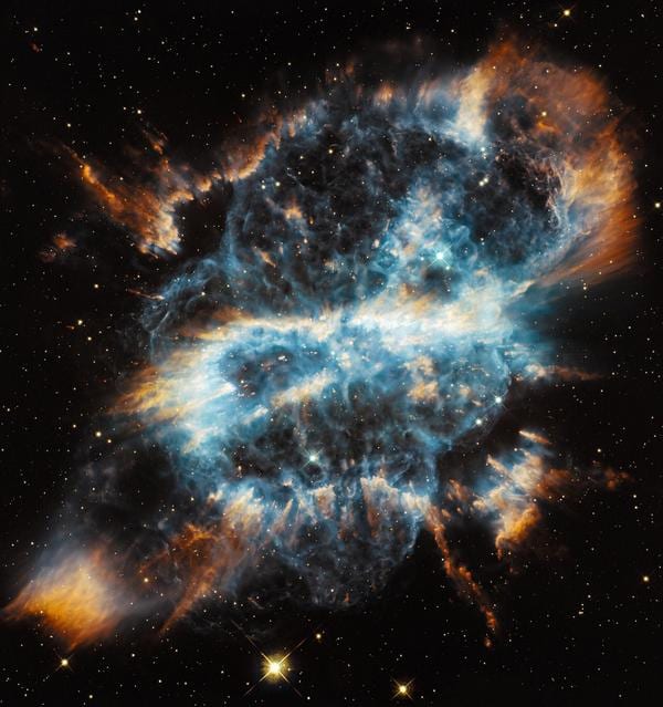Planetary nebula of blue and orange gas filaments bursting outward against a starry black sky