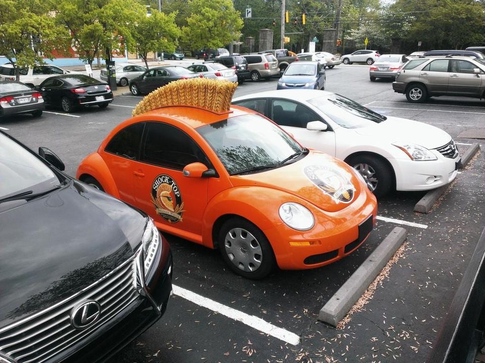 Orange Shock Top Volkswagen Beetle with a giant golden wheat mohawk on its roof in a parking lot