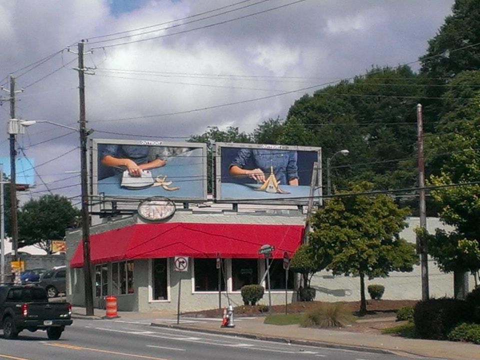 Two billboards above a red-awninged shop showing hands ironing and then folding a banana peel on a blue table