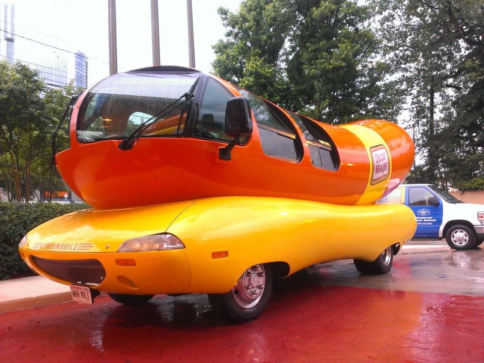 Oscar Mayer Wienermobile parked on wet red pavement with a WNR MBLE license plate