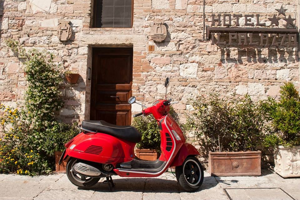 Red Vespa scooter parked in front of the stone facade of Hotel Il Palazzo in Italy