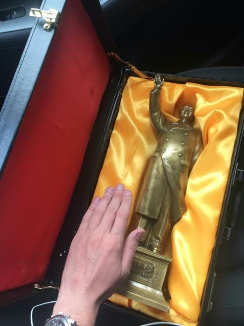 Hand beside a brass statue of Chairman Mao waving in a case lined with gold satin