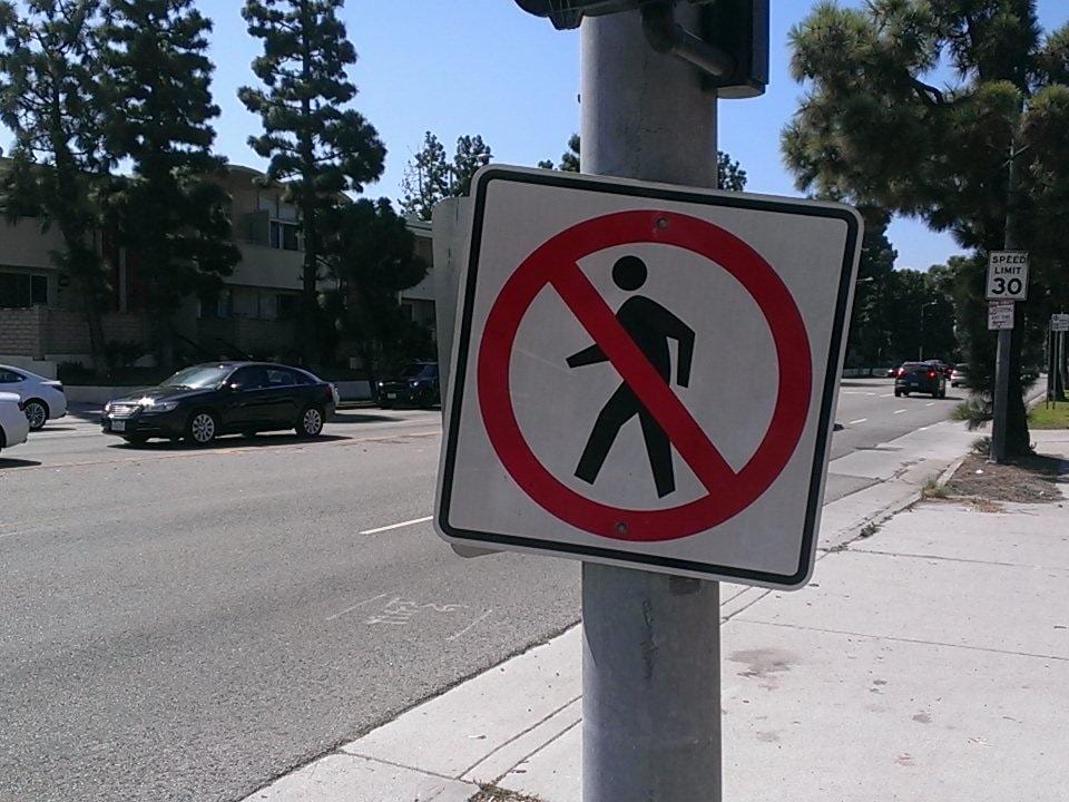 No pedestrian crossing sign on a pole beside a wide Los Angeles street with a 30 mph speed limit sign