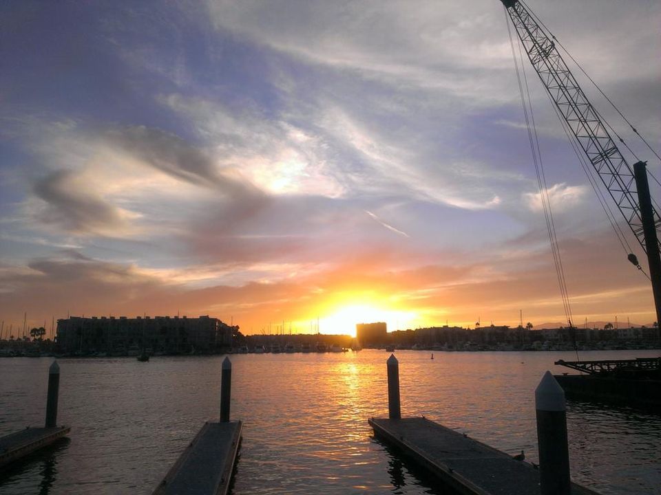Orange sunset over a marina with floating docks in the foreground and a construction crane at right