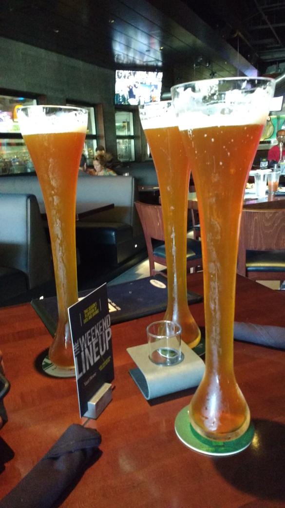 Three tall yard glasses of amber beer on a sports bar table