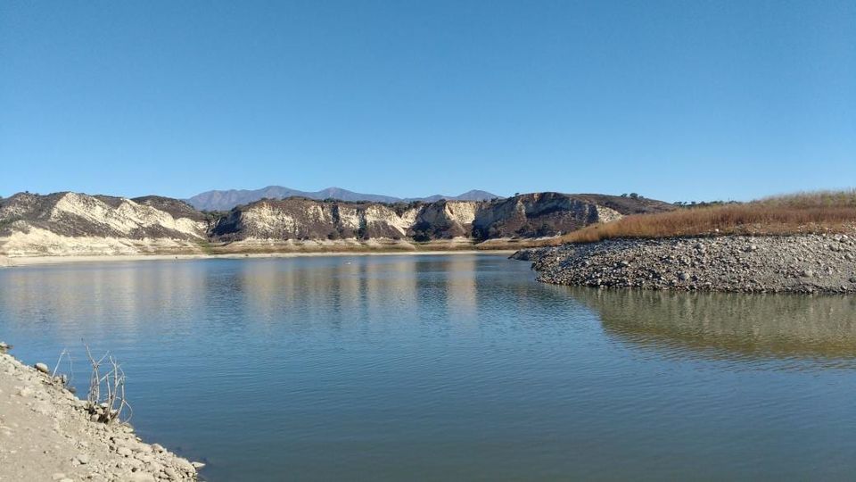 Low lake water beneath pale exposed cliffs and distant mountains under a clear sky
