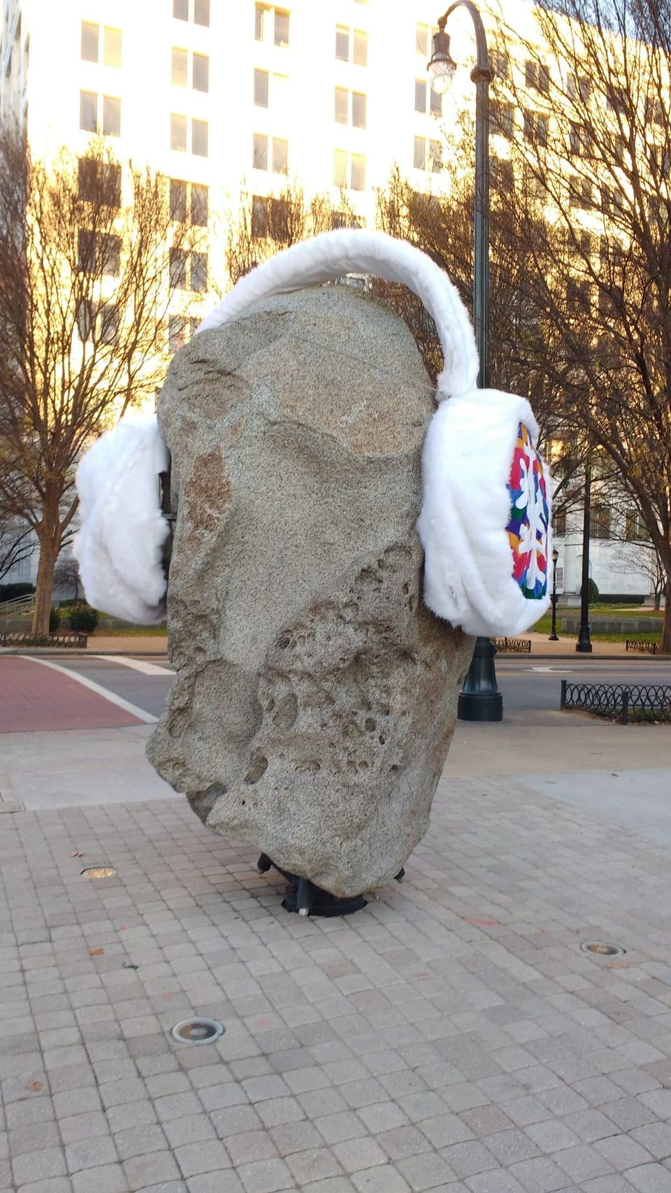 Large granite rock sculpture on a plaza wearing oversized white fuzzy earmuffs