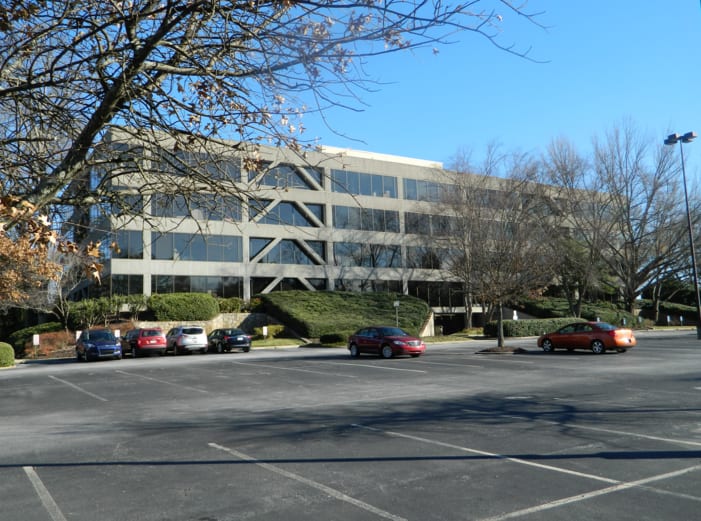 Four-story suburban office building with a mostly empty parking lot and bare trees