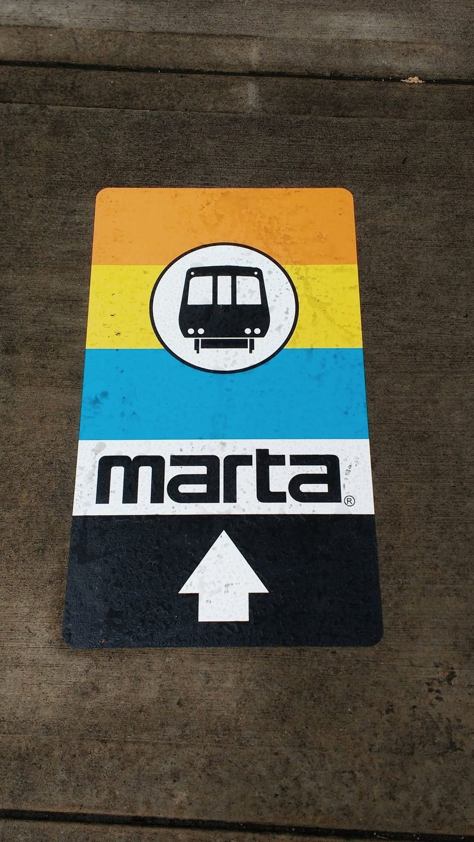 Sidewalk decal with orange, yellow and blue stripes, a train icon, the MARTA logo and an up arrow