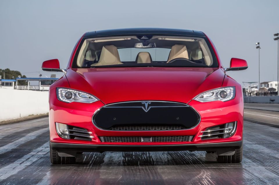 Front view of a red Tesla Model S showing its black nose cone and T logo on a drag strip