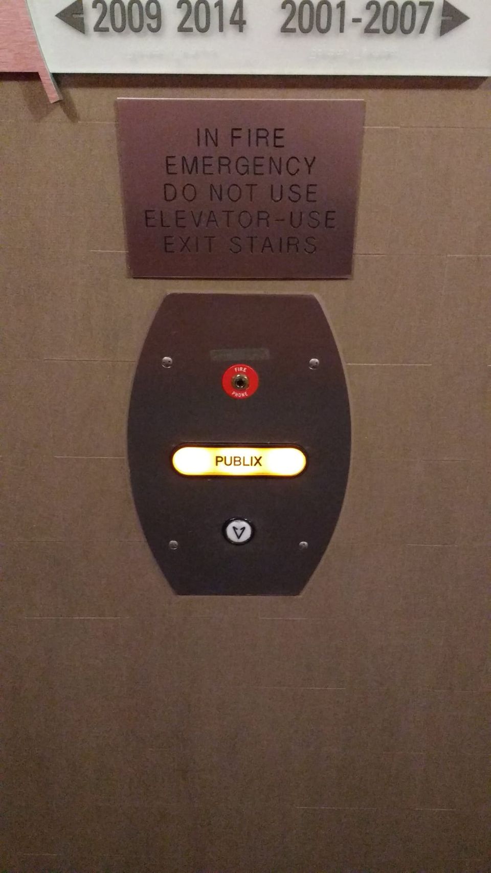 Elevator call panel with a single glowing button labeled Publix below a fire emergency sign