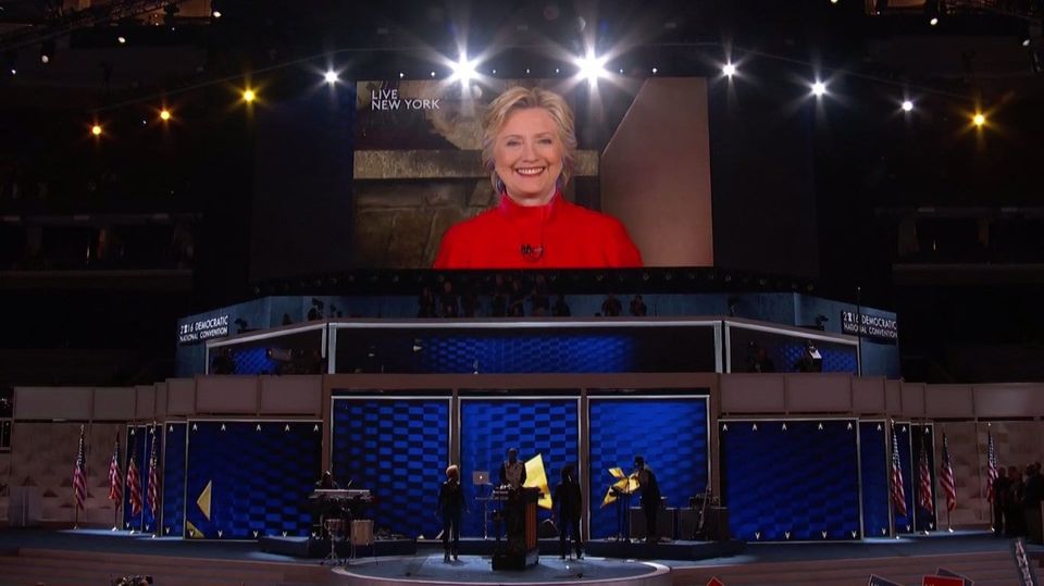 Hillary Clinton smiling on a giant screen labeled Live New York above the 2016 Democratic National Convention stage