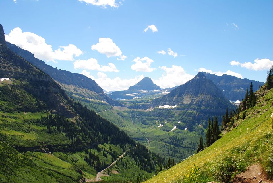 Green glacial valley with Going-to-the-Sun Road winding below pyramid peaks and puffy clouds in Glacier National Park