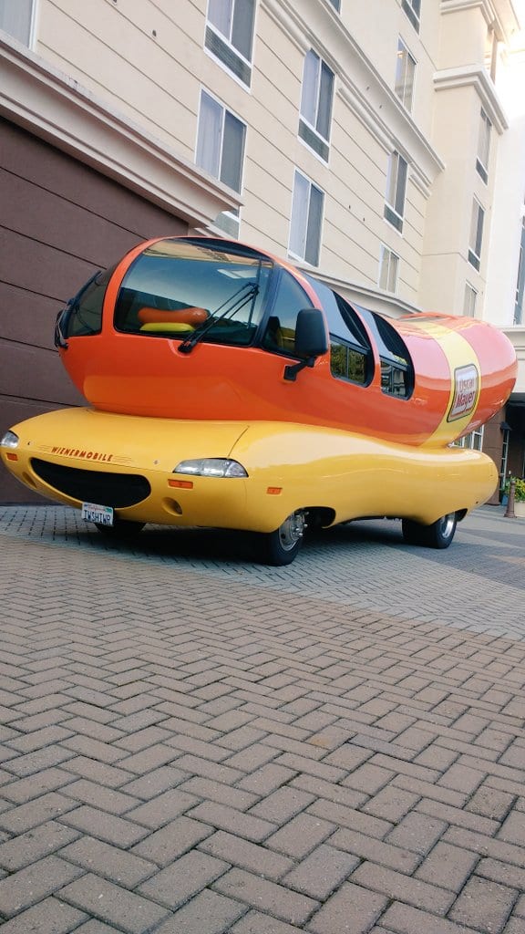 Oscar Mayer Wienermobile hot dog vehicle parked on a brick driveway in front of a hotel