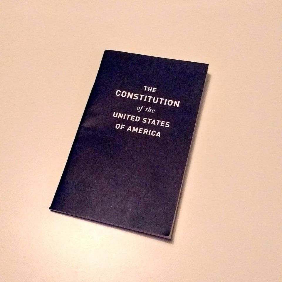 Navy pocket booklet titled The Constitution of the United States of America on a tan table