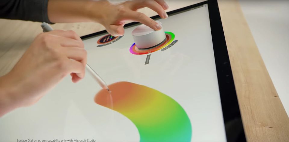 Hands using a pen and the Surface Dial on a Surface Studio screen to paint a rainbow gradient stroke