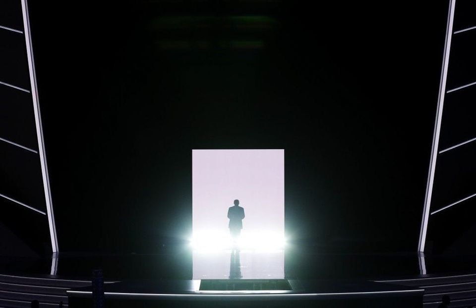 Silhouette of a man walking toward a glowing doorway on a dark convention stage