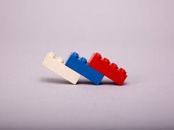 White, blue and red LEGO bricks leaning together on a gray background