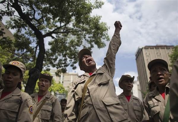 Venezuelan militia members in tan uniforms and hats chanting as one raises a fist
