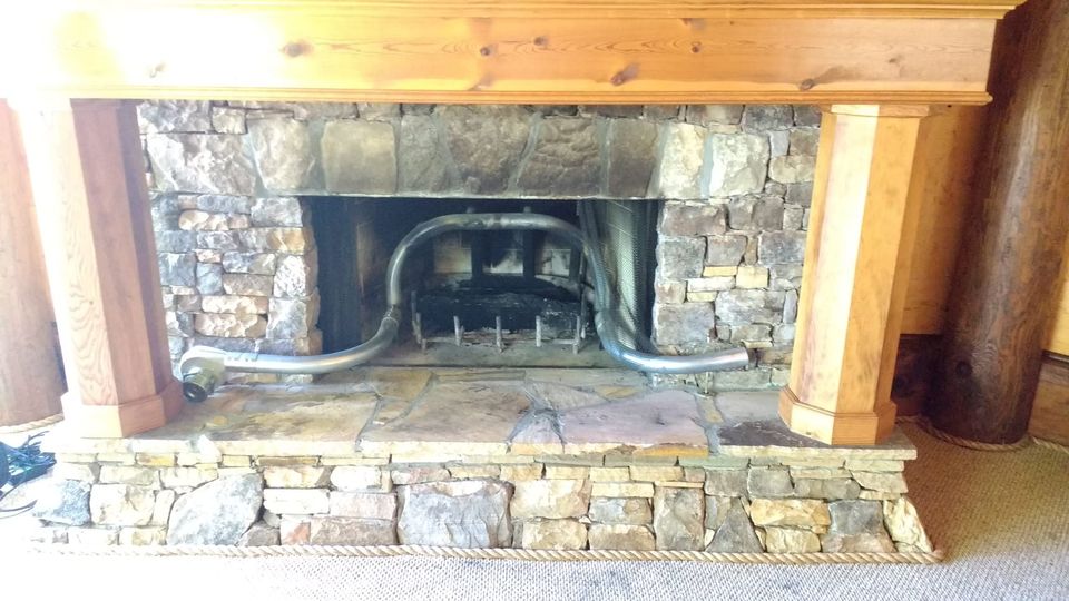 Stone fireplace with wooden columns and a curved metal blower pipe arching over the grate