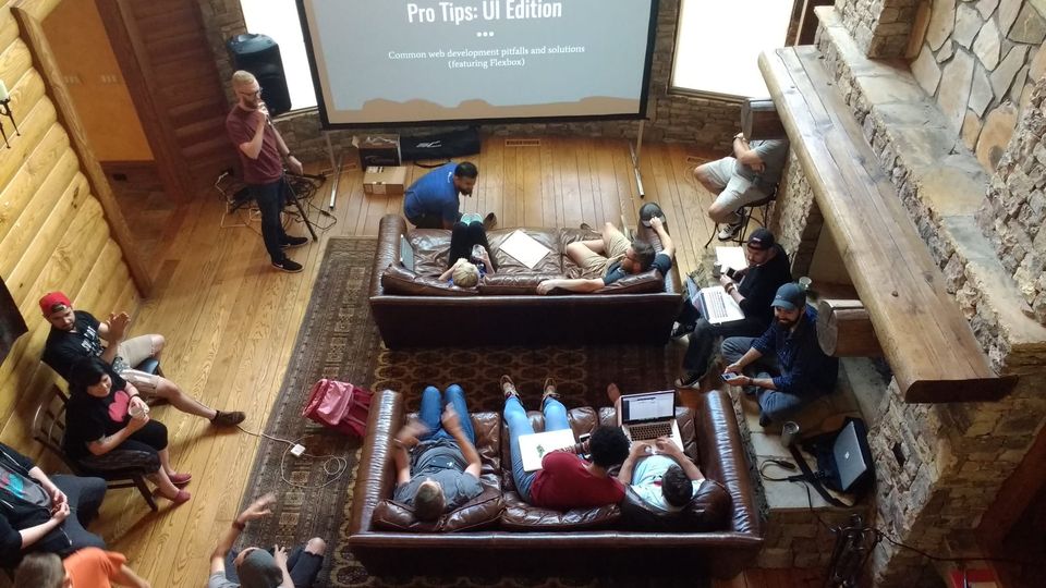Overhead view of a man presenting Pro Tips: UI Edition on a screen to coworkers on leather couches in a log cabin