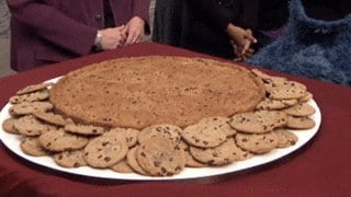 Platter of chocolate chip cookies surrounding one giant cookie with a blue furry arm reaching in
