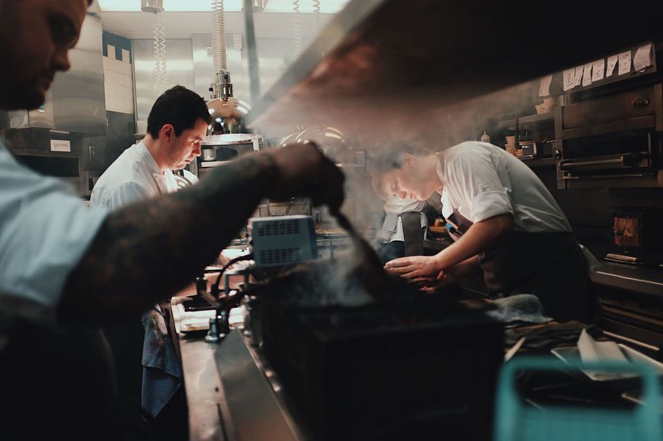 Chefs in white jackets working in a smoky restaurant kitchen