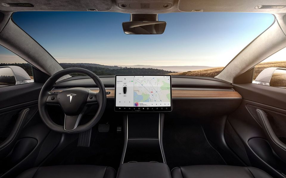 Tesla Model 3 interior with a bare dashboard, wood trim and a single center touchscreen showing a map