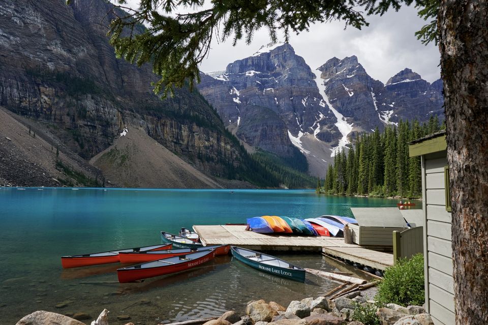 Red and green Moraine Lake Lodge canoes by a dock on turquoise water below jagged snowy peaks