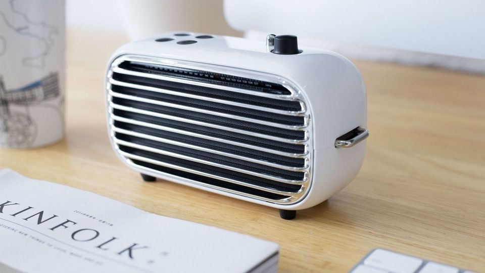 White retro radio-style wireless speaker with a chrome grille on a wooden desk beside a Kinfolk magazine