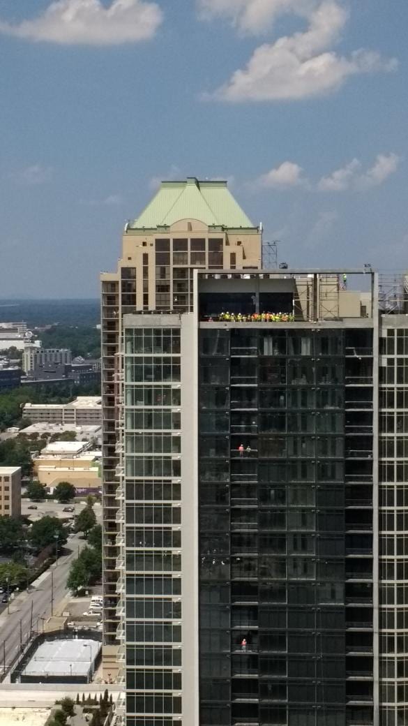 Construction workers in yellow vests lined up on top of a glass high-rise under construction in Atlanta